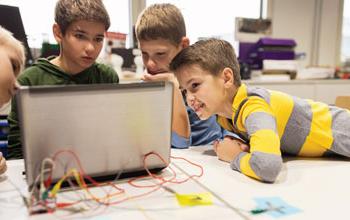 4个孩子看着电脑，电脑后面的面板上插着五颜六色的电线.