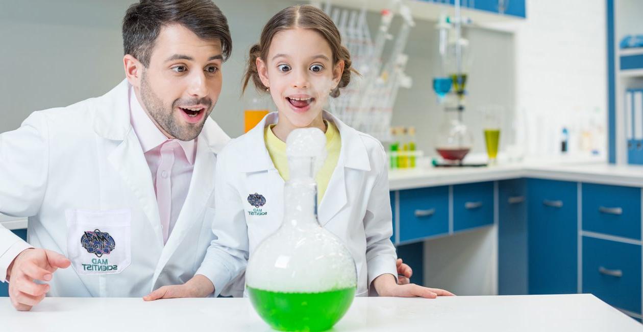 科学家和小女孩在实验室里看着一个瓶子，里面有绿色的液体.